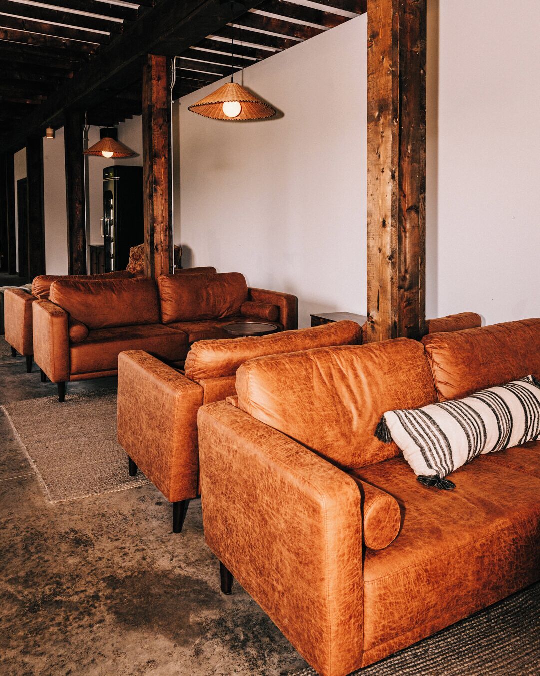 A modern living room with leather sofas, wooden beams, and hanging lamps.