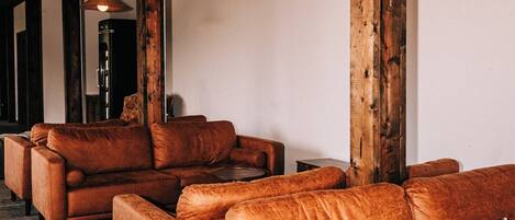 A modern living room with leather sofas, wooden beams, and hanging lamps.