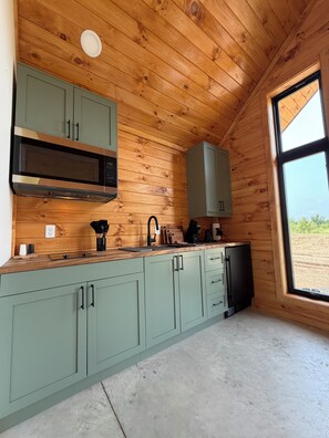 A kitchen with wooden ceiling, green cabinets, a microwave, and a window with a view. - Off Map (South Haven)