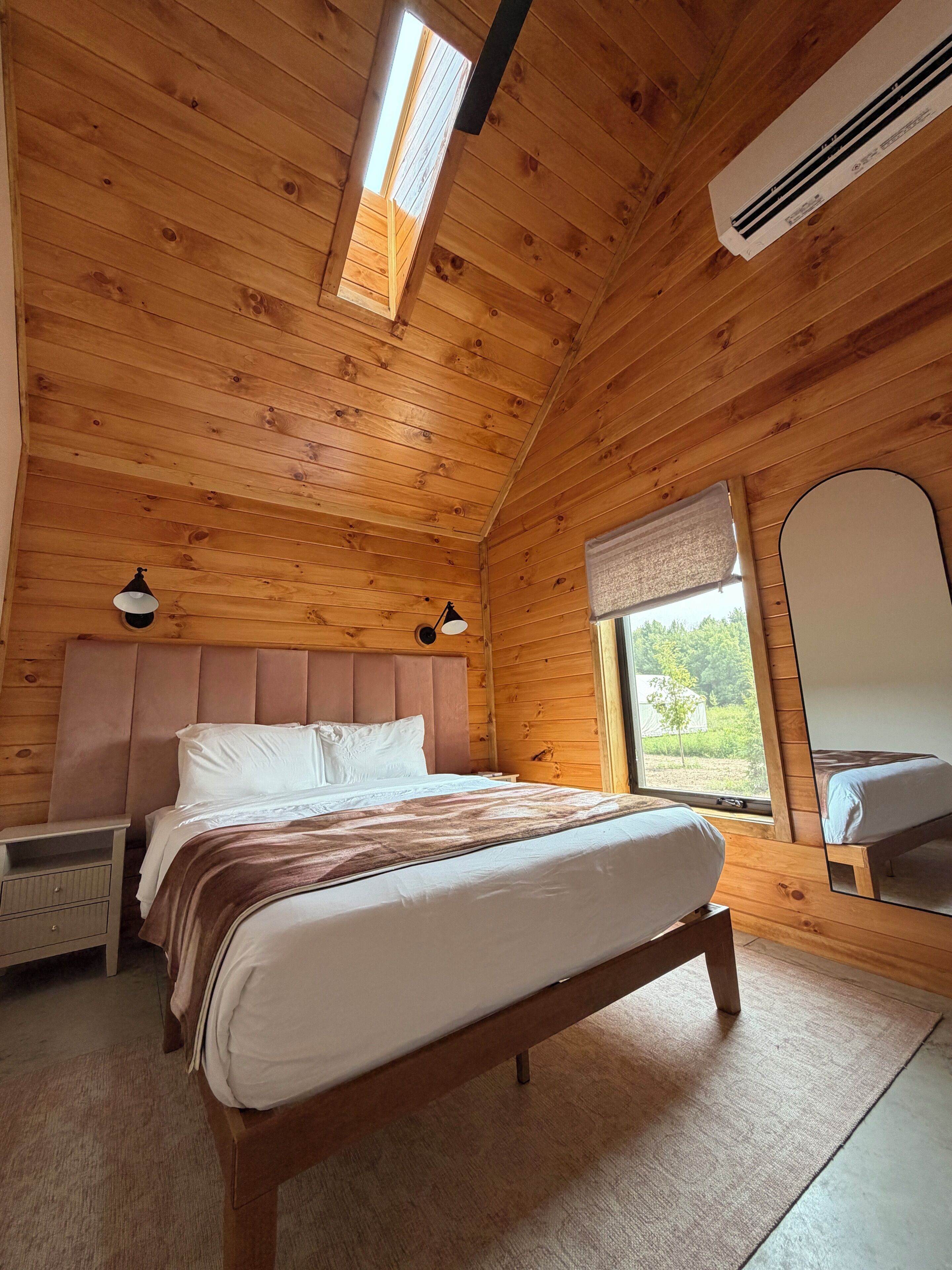 A wooden-paneled bedroom with a bed, bedside tables, and a window with a view.