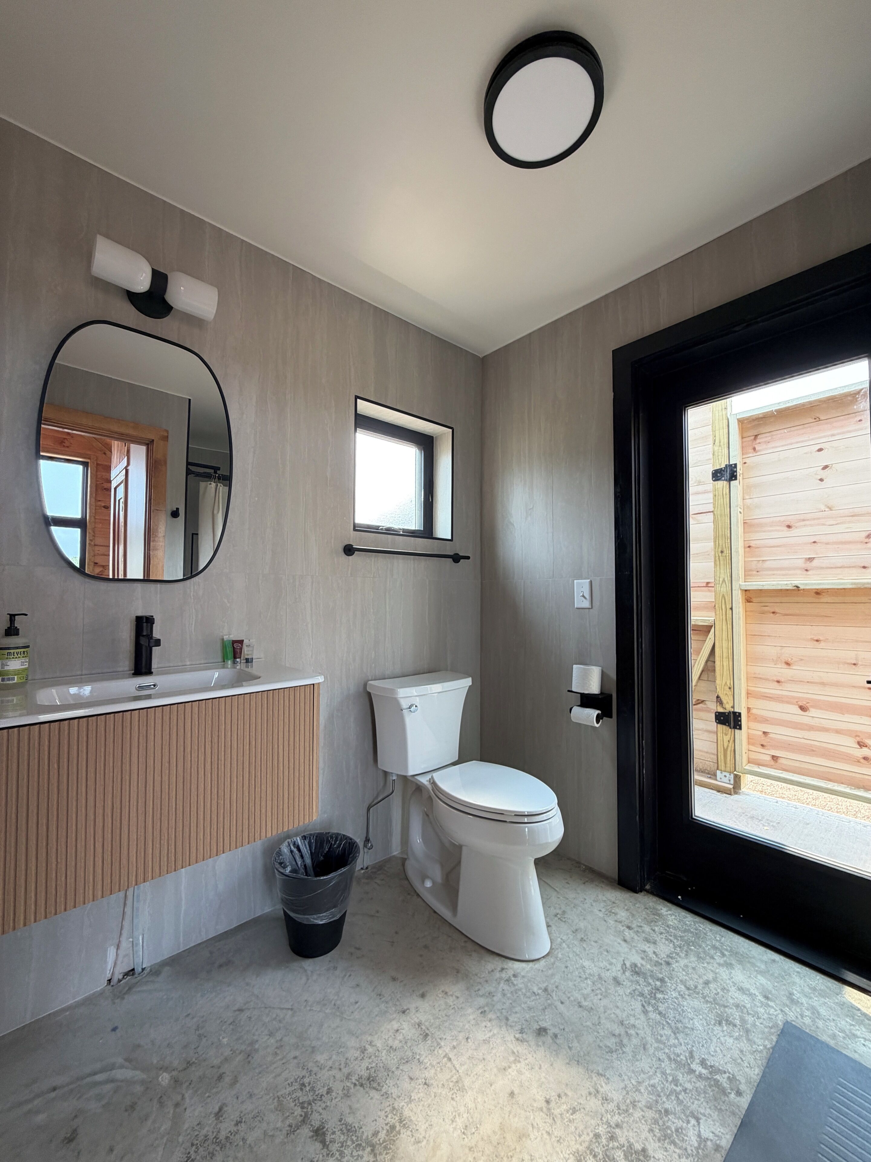 A modern bathroom with a toilet, sink, mirror, and window.