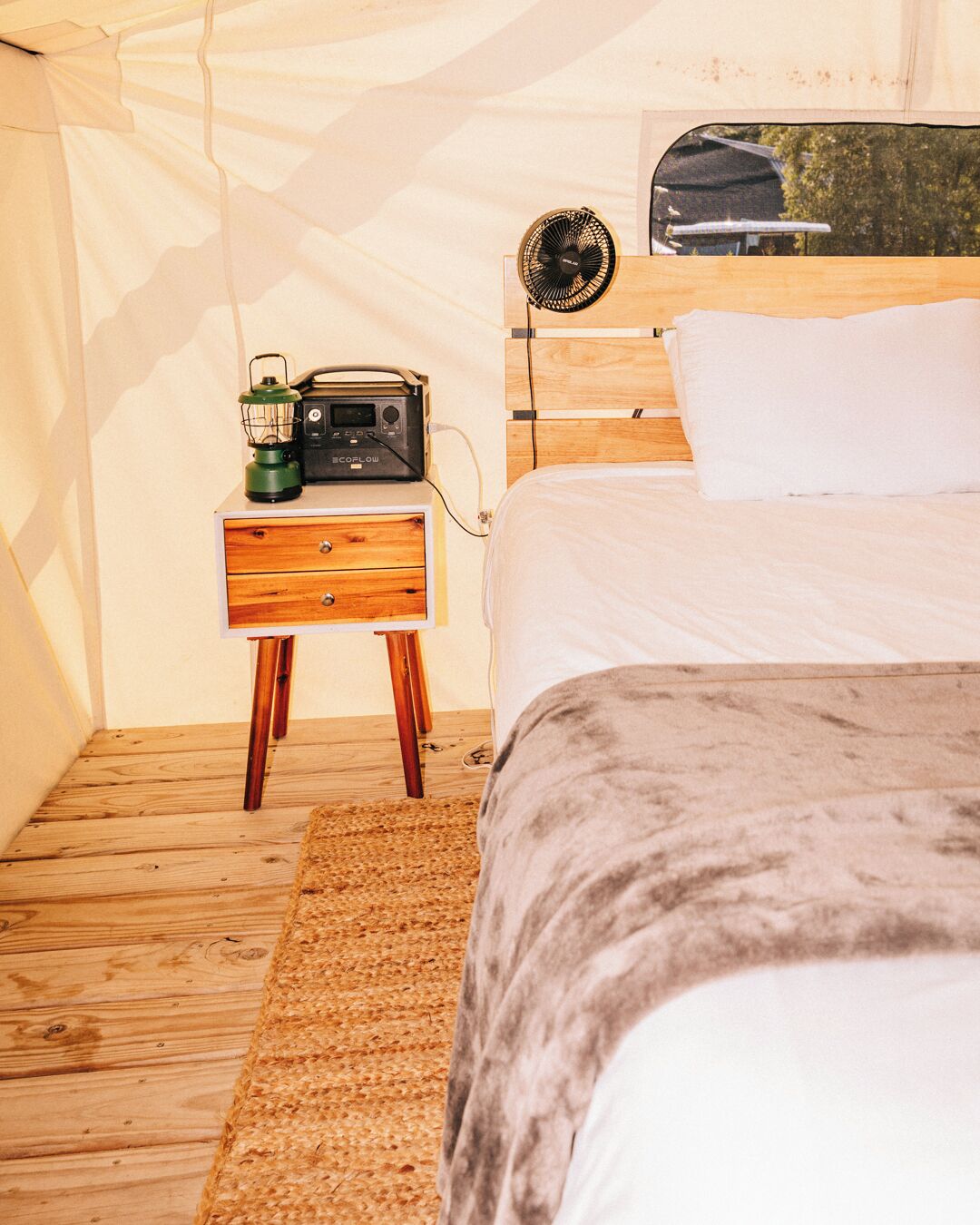 A cozy bedroom with a wooden bed, a nightstand with a radio and lantern, and a view of a building through a window.