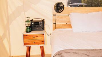 Ein gemütliches Schlafzimmer mit einem hölzernen Bett, einem Nachttisch mit Radio und Laterne und Blick auf ein Gebäude durch ein Fenster.