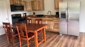 A modern kitchen with wooden cabinets, a stainless steel refrigerator, a stove, and a dining table with chairs.