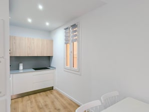 Une petite cuisine avec des meubles en bois, une fenêtre avec des stores, un plan de travail blanc et un plancher en bois.