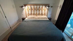Ein Schlafzimmer mit Bett, Holzkopfteil, Nachttischen und einem Fenster mit Blick.