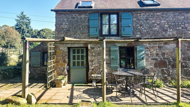 Une maison en pierre avec un patio, une porte et une fenêtre équipée de volets.