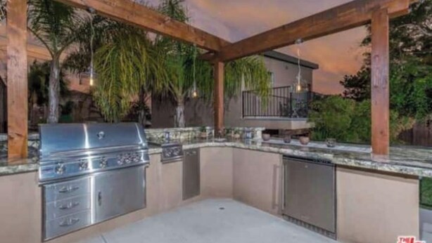 Eine Außenküche mit Edelstahlgrill, eingebauten Schränken und einer Holzpergola.