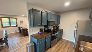 A modern kitchen with grey cabinets, a wooden countertop, stainless steel appliances, and a sign above the cabinets reading "OUR HAPPY PLACE".
