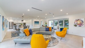 Un salon moderne avec un canapé d’angle gris, un fauteuil jaune et un coin repas comprenant une table et des chaises.