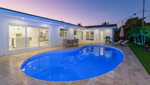 Une maison moderne dotée d’une piscine, d’un coin repas et d’une terrasse avec des chaises longues.