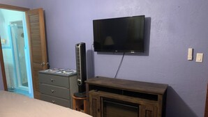 Un dormitorio con una cama, un aparador, un televisor montado en la pared y un mueble pequeño con un acuario.