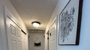 Un couloir étroit, avec des portes blanches de chaque côté, un plancher en bois et un luminaire au plafond.