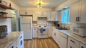 Une cuisine moderne avec des meubles blancs, un îlot central, une cuisinière et un four à micro-ondes.