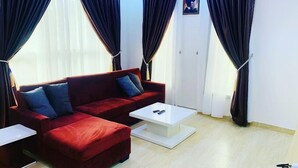 A living room with a red sofa, white coffee table, and dark curtains. - Quayy Apartments and Suites (Abuja)