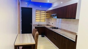 A modern kitchen with wooden cabinets, a countertop, a sink, and a window with blinds. - Quayy Apartments and Suites (Abuja)