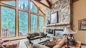 Un salón espacioso con ventanas amplias, una chimenea de piedra y una zona de estar acogedora.