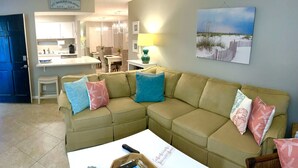 A living room with a beige sectional sofa, a coffee table, and a painting of a beach scene.