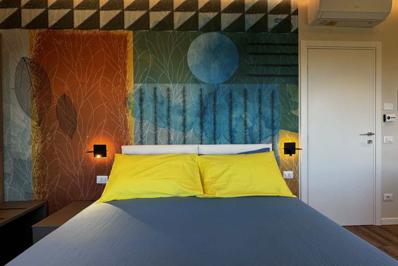Una cama con almohadas amarillas, cabecera y pared con diseño geométrico y un motivo circular.