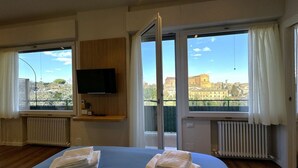 A hotel room with a bed, a TV mounted on the wall, and large windows offering a city view. - Skyline-Bluemoon ( studio apartment with a view) (Siena)