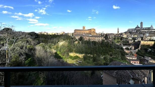A historic building with a prominent tower, surrounded by dense forest and urban structures. - Skyline-Bluemoon ( studio apartment with a view) (Siena)