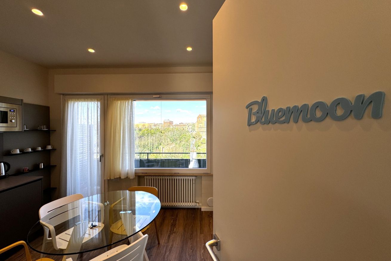 Een moderne hotelkamer met een glazen eettafel, een magnetron en uitzicht op de stad door grote ramen.