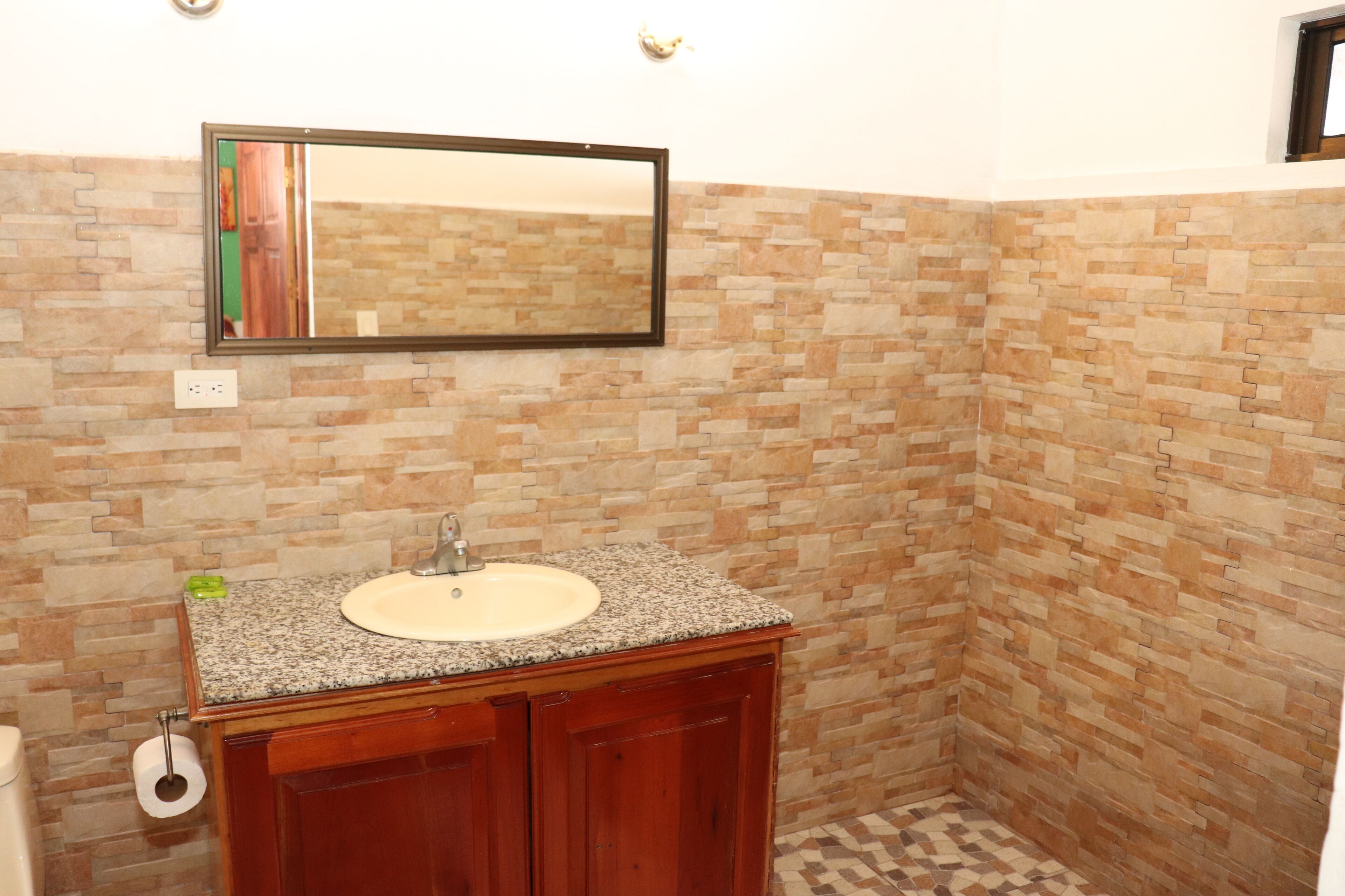 A bathroom with a granite countertop sink, wooden cabinets, a mirror, and a tiled floor.