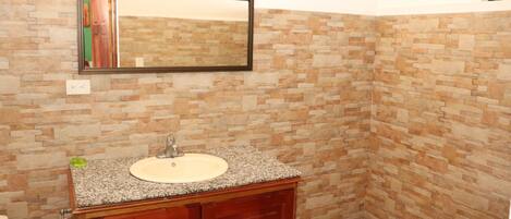 A bathroom with a granite countertop sink, wooden cabinets, a mirror, and a tiled floor.