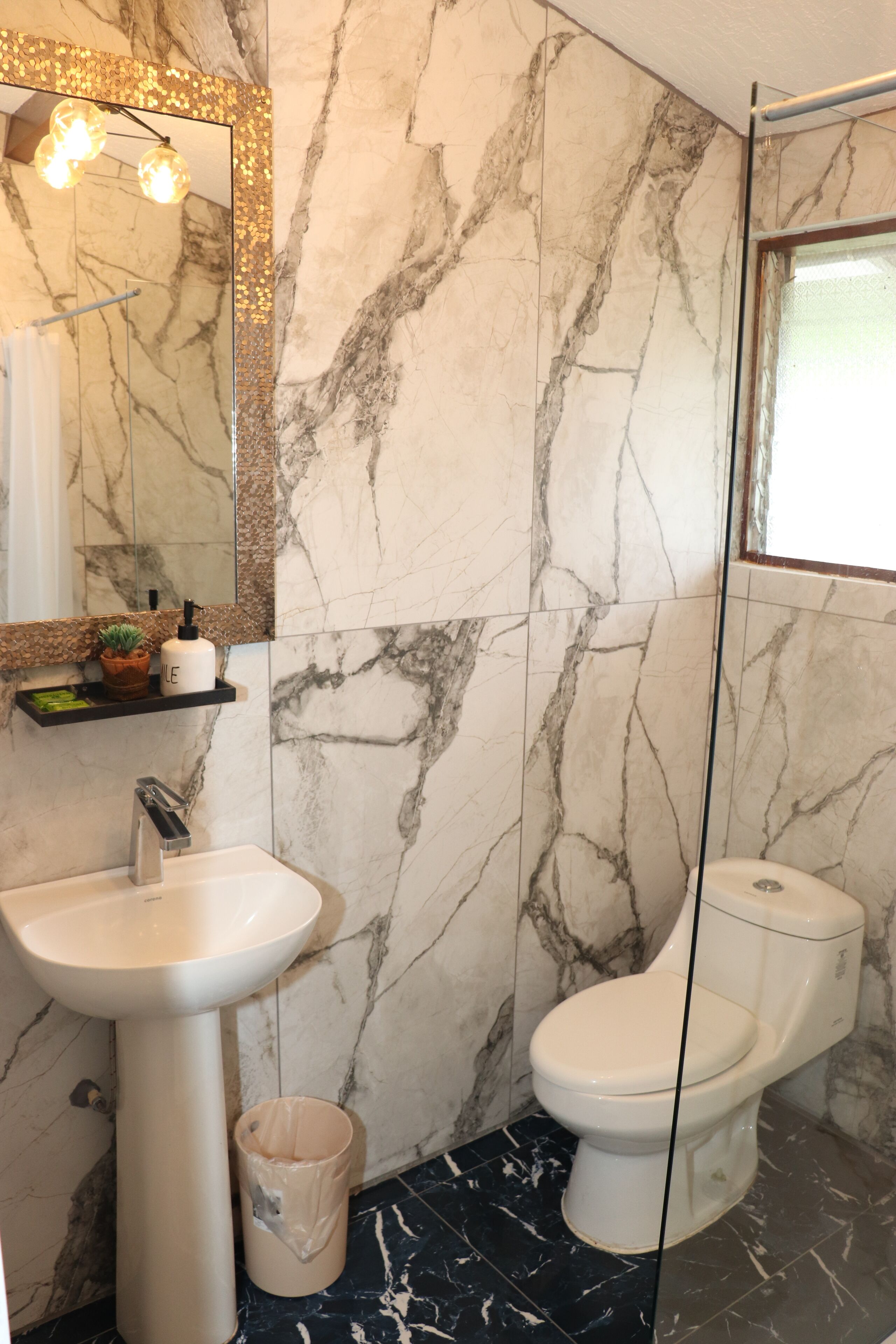 A bathroom with a marble wall, a sink, a toilet, and a mirror with lights.