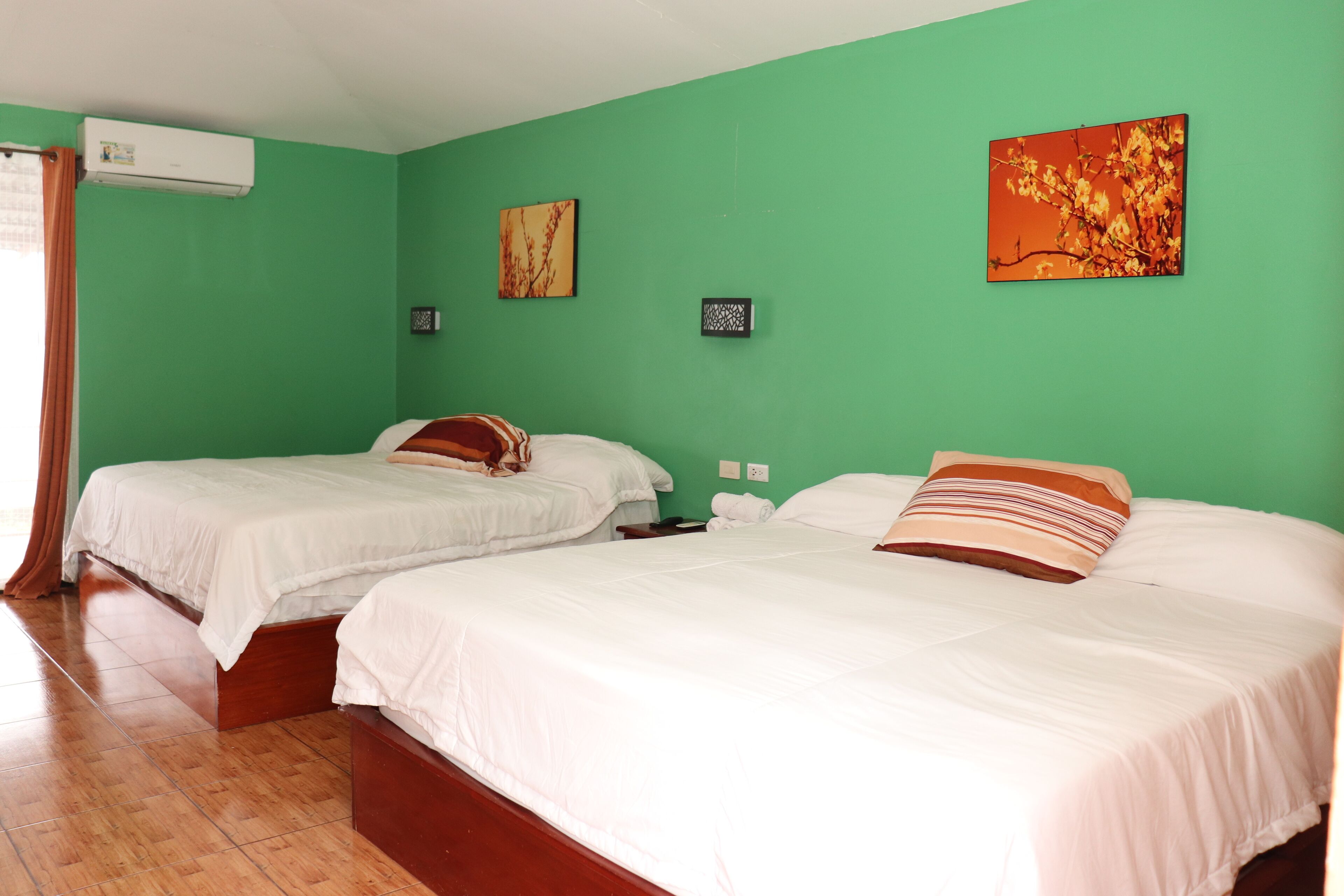 Una habitación con dos camas, paredes verdes y piso de madera.