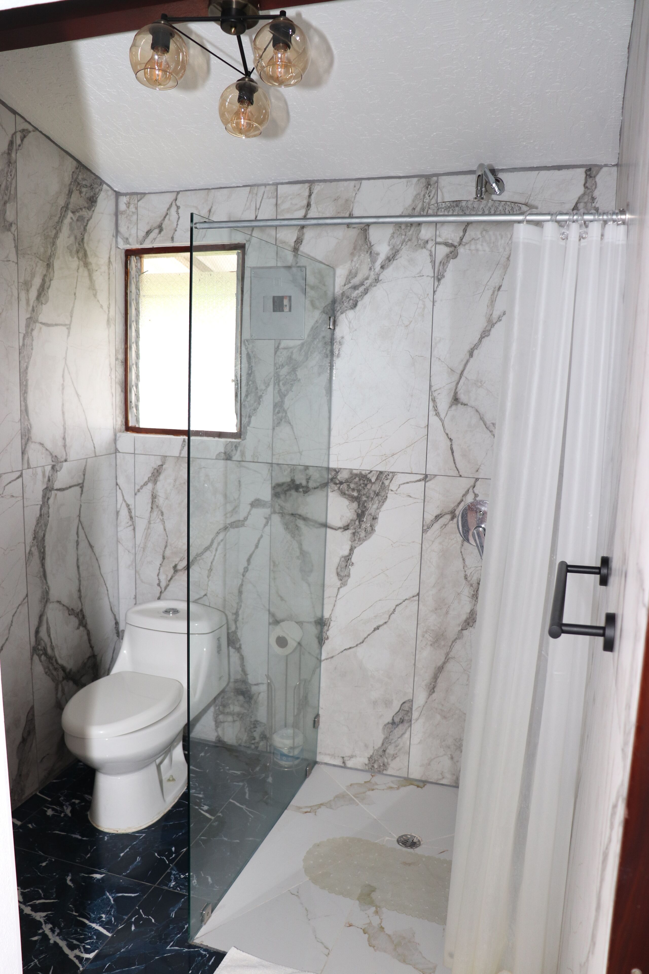A bathroom with a glass-enclosed shower, a toilet, and a marble-tiled wall.