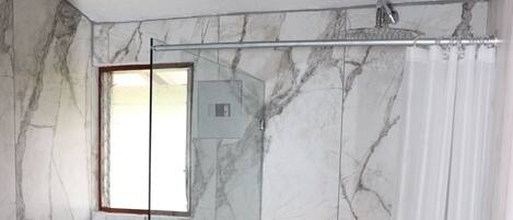 A bathroom with a glass-enclosed shower, a toilet, and a marble-tiled wall.