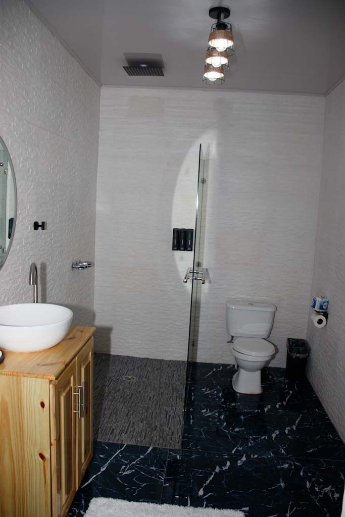 A bathroom with a white sink, wooden cabinet, glass shower enclosure, white toilet, and a marble floor.