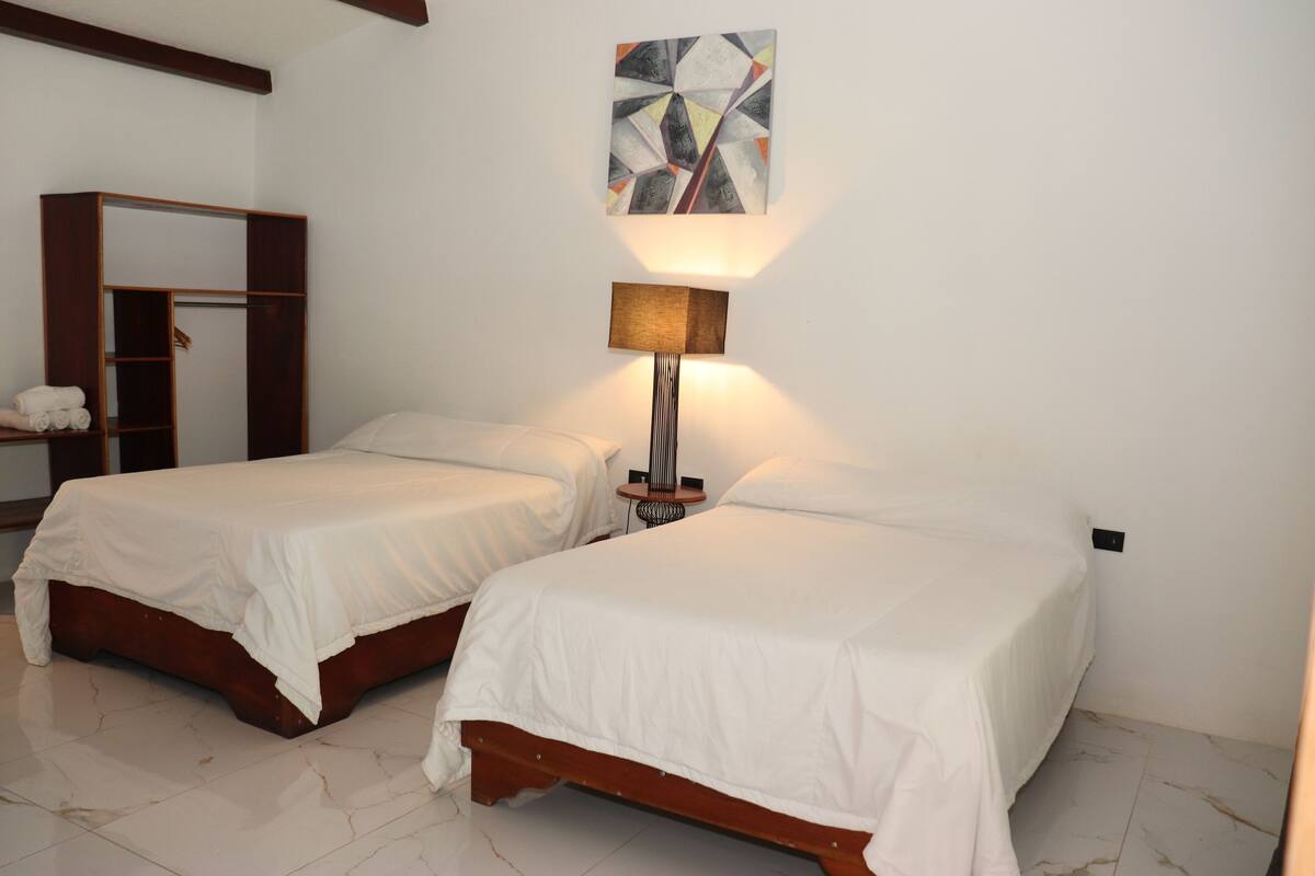 A bedroom with two beds, a wardrobe, a lamp, and a wall art piece.