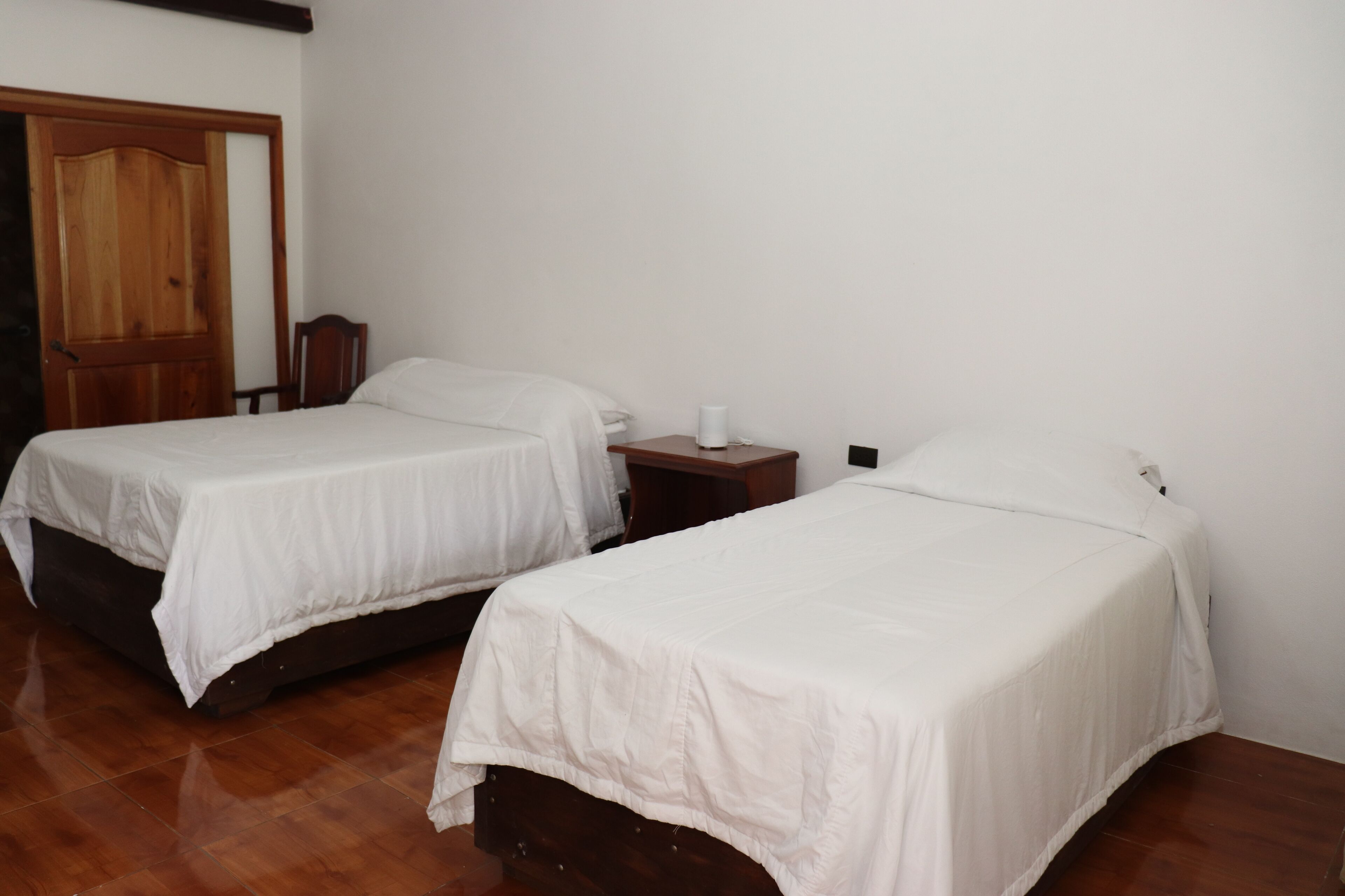 Two single beds with white linens in a room with wooden flooring and a wooden door.