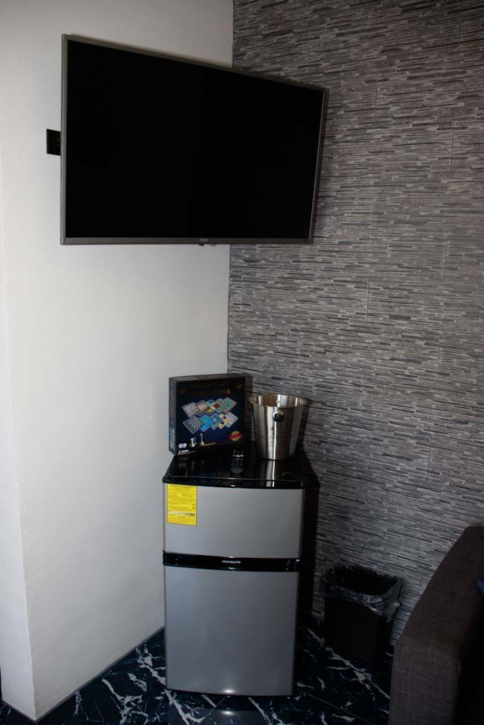 Eine kompakte Küchenzeile mit Kühlschrank, Mikrowelle und kleinem Spülbecken. Ein Flachbildfernseher ist an der Wand über der Arbeitsfläche angebracht.