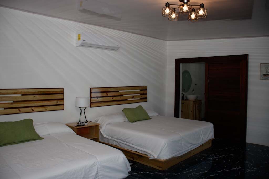 A hotel room with two beds, wooden headboards, a nightstand with a lamp, a marble floor, and a ceiling light fixture.