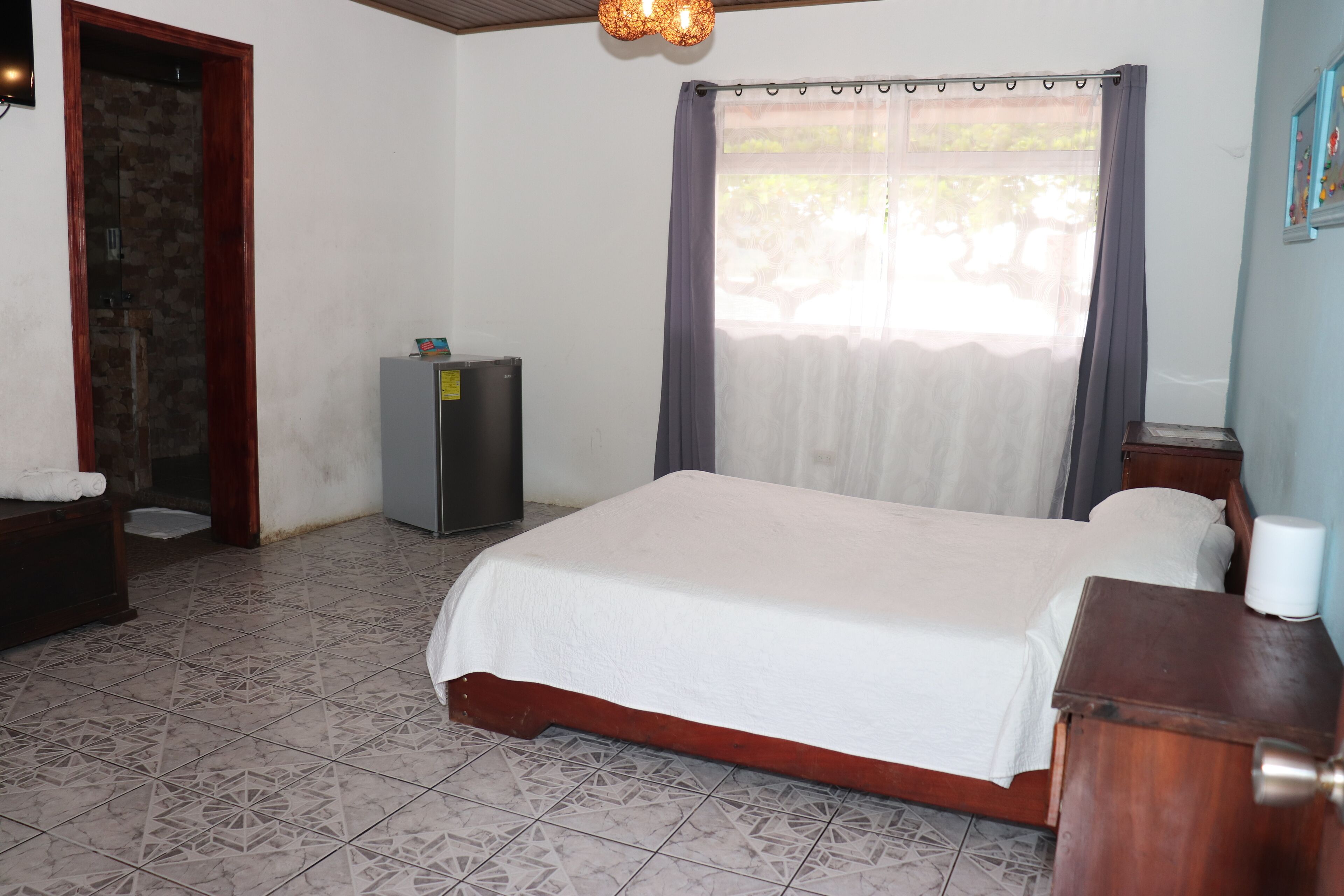 A bedroom with a bed, a small cabinet, a television, and a window with curtains.