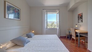 Quarto com cama, escrivaninha, cadeira, janela com cortinas e um cartaz na parede.