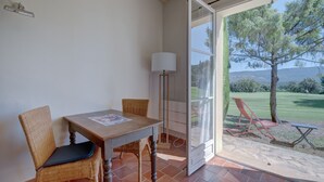 Uma área de refeições com mesa e cadeiras, uma luminária e vista para uma área gramada com árvores e colinas.