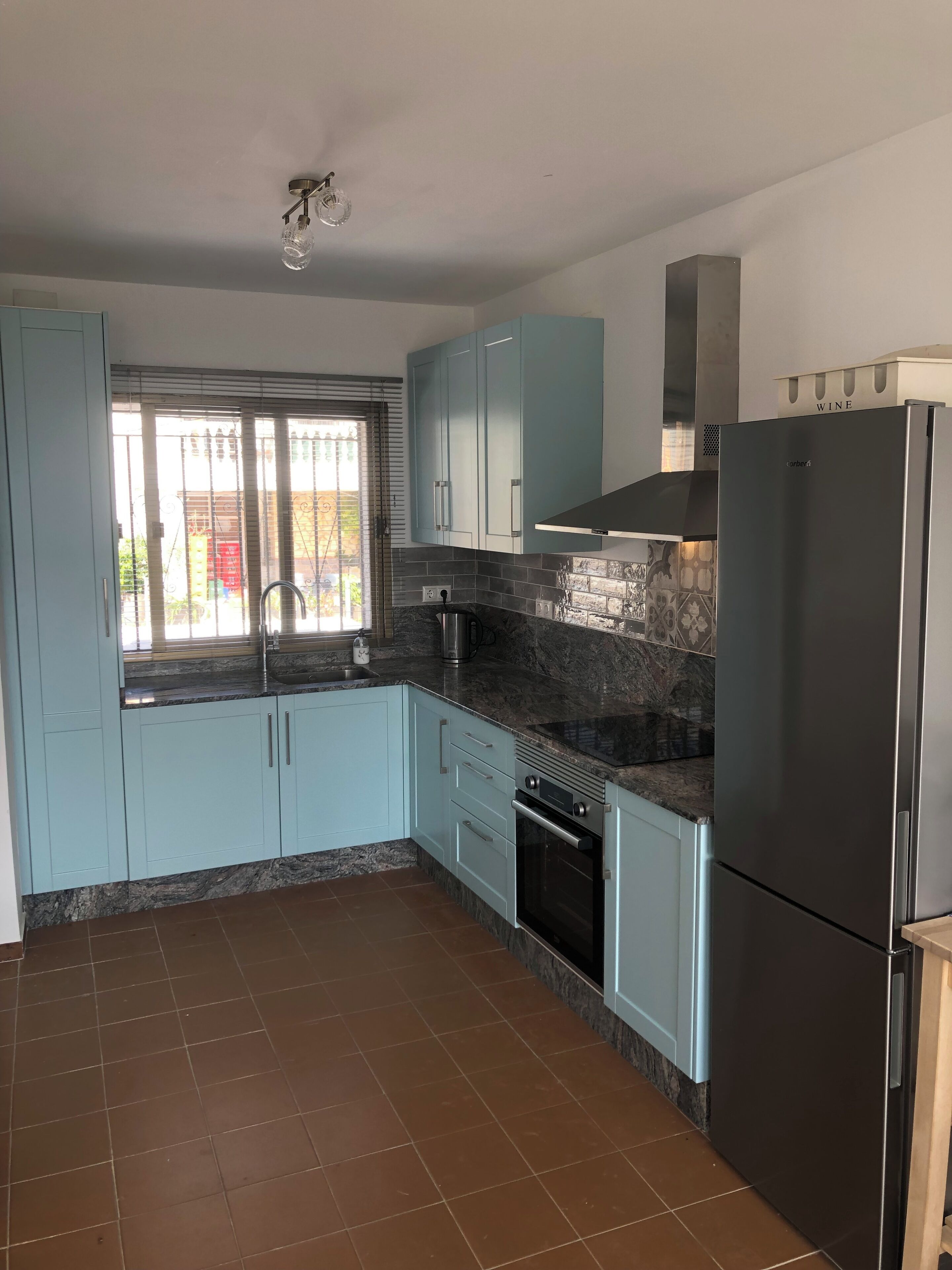 A kitchen with light blue cabinets, a black refrigerator, and a tiled backsplash.