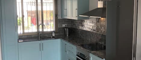A kitchen with light blue cabinets, a black refrigerator, and a tiled backsplash.