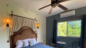 A bedroom with a bed, bedside lamps, a ceiling fan, a window, and a small table with chairs.