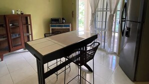 Una cocina con mesa, sillas, ventilador de techo, refrigerador y ventana con cortinas.