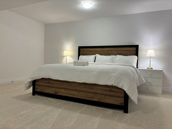 A neatly made bed with a wooden headboard, two bedside lamps, and a white nightstand with drawers.