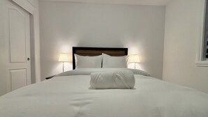 A neatly made bed with white linens and a rolled towel, two bedside lamps, and a wooden headboard.