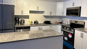 A modern kitchen with white cabinets, a stainless steel refrigerator, a microwave, a stove, and a dishwasher.