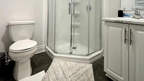 A bathroom with a glass-enclosed shower, a white toilet, and a marble-tiled floor.