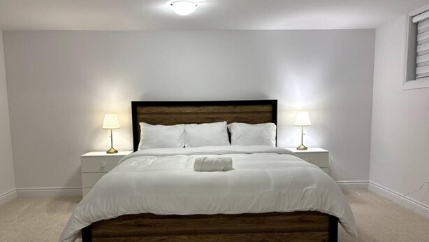 A bedroom with a wooden bed frame, white bedding, two bedside lamps, and a small bedside table.