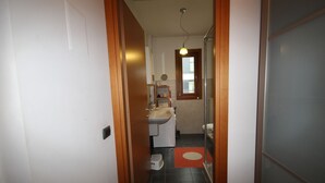A narrow hallway leading to a bathroom with a sink, mirror, and window. - Cola Montano Apartment (Milano)